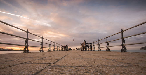 People on bridge against sky during sunset