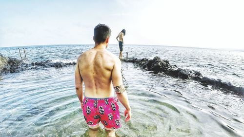 Rear view of shirtless man looking at sea against sky