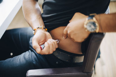 Midsection of businessman injecting insulin in abdomen while sitting at table in office