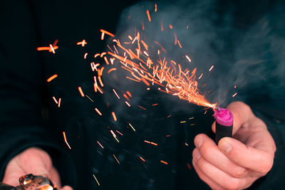 Cropped image of hand holding sparkler against fire