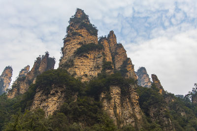 Low angle view of cliff against cloudy sky