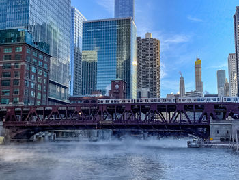 Bridge over river by buildings against sky in city