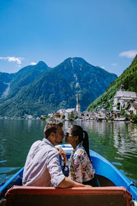 Couple sitting on mountain by lake against mountains