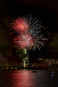 Firework display over illuminated city against sky at night