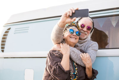 Smiling senior couple doing selfie while standing by van outdoors