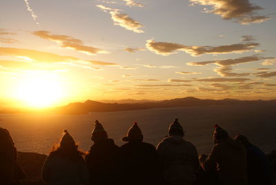 People on shore against sky during sunset