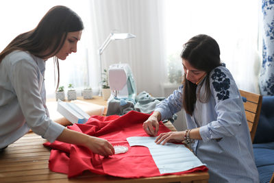 Women work with patterns and fabric, pinning patterns to a red canvas, close-up, top view.
