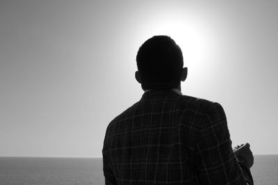 Rear view of man standing at beach against clear sky