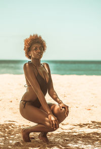 Young woman sitting on shore at beach against sky