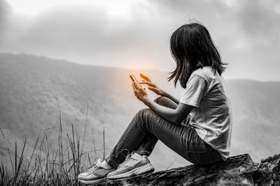 Side view of woman sitting against mountains against sky