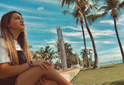 Beautiful woman sitting on palm trees at beach against sky
