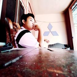 Boy looking away while sitting on table at home