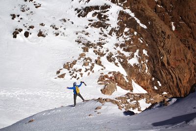 High angle view of man with arms outstretched standing on snowcapped mountain