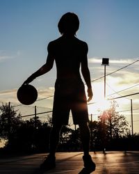 Rear view of silhouette woman standing by ball against sky during sunset