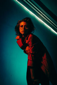 Portrait of young woman standing against illuminated wall