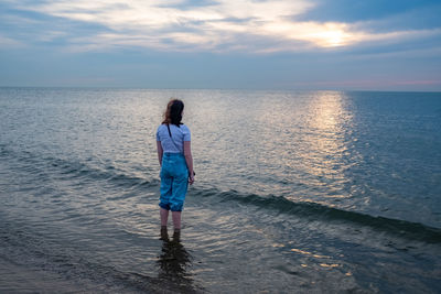 Rear view of woman standing at beach against sky