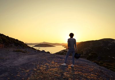 Rear view of hiker standing on mountain against sky during sunset