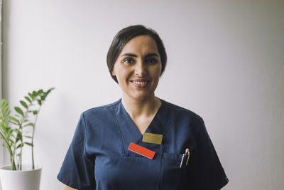 Portrait of smiling confident female nurse against wall at hospital