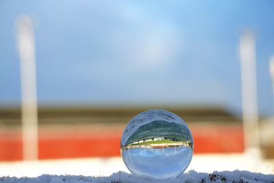 Close-up of crystal ball on glass against blue sky