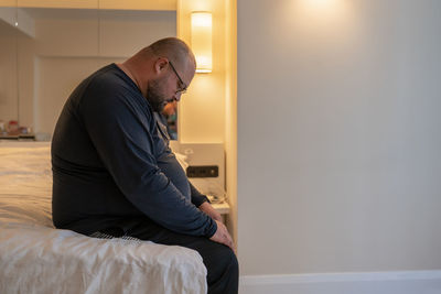 Side view of young man sitting on bed at home