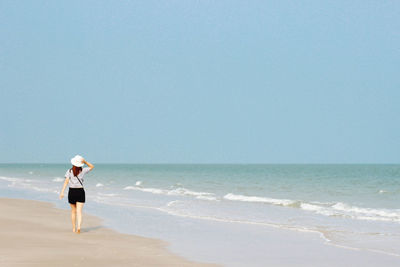 Rear view of woman standing on beach against clear sky