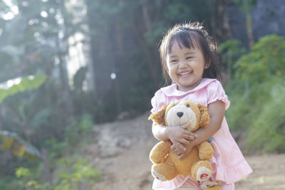 Cute girl holding teddy bear while standing outdoors