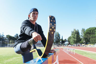 Young athlete stretching prosthetic leg on railing at running track