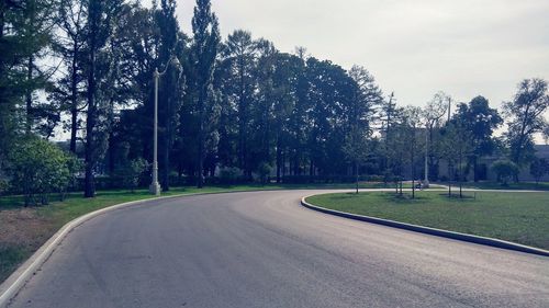 Empty road by trees in city against sky