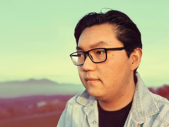 Close-up of man in eyeglasses against sky