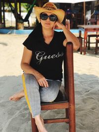 Portrait of woman in sunglasses and hat siting on chair at beach