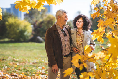  a mature couple, embracing, communicates under a tree in an autumn park.