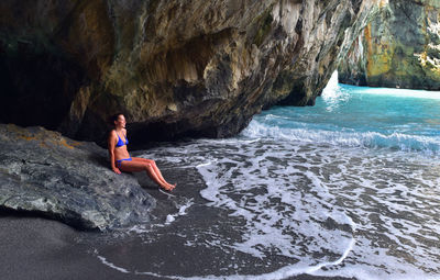 Mid adult woman in bikini sitting on rock at beach