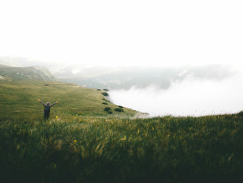 High angle view of female hiker with arms raised standing on mountain during foggy weather