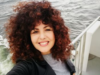 Portrait of smiling woman with curly hair in boat at sea