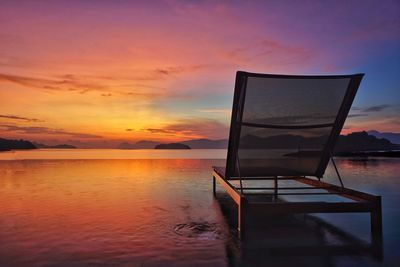 Lounge chair in infinity pool by sea against orange sky