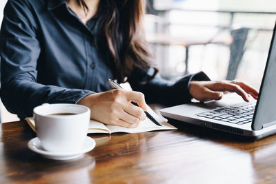 Midsection of woman holding coffee cup on table