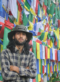 A young guy looking at camera posing with his arms crossed, standing against buddhist prayer flags