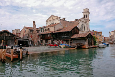 Sailboats in canal by buildings in city against sky