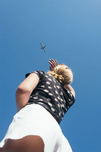 Low angle view of woman shielding eyes while looking at airplane