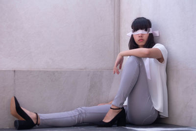 Young woman with blindfold sitting on floor against wall
