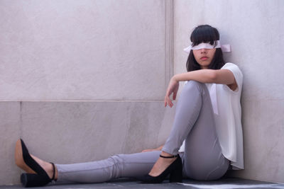 Young woman sitting against wall