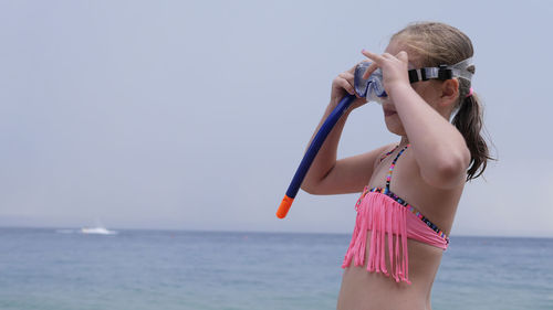 Girl wearing swimming goggles at beach against sky