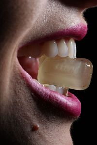 Midsection of woman holding candy through mouth against black background