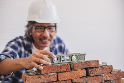 Mature man wearing hardhat making brick wall in workshop