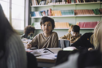 Portrait of boy sitting on desk in classroom at school