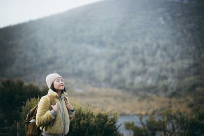 Smiling woman with eyes closed standing against mountain
