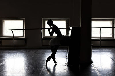 Full length of silhouette ballet dancer standing by window