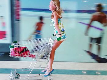 Full length of happy girl riding on shopping cart in shopping mall