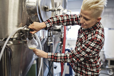 Confident female manager pouring beer from storage tank at factory