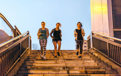 Women friends training running down stairs in town on sunset